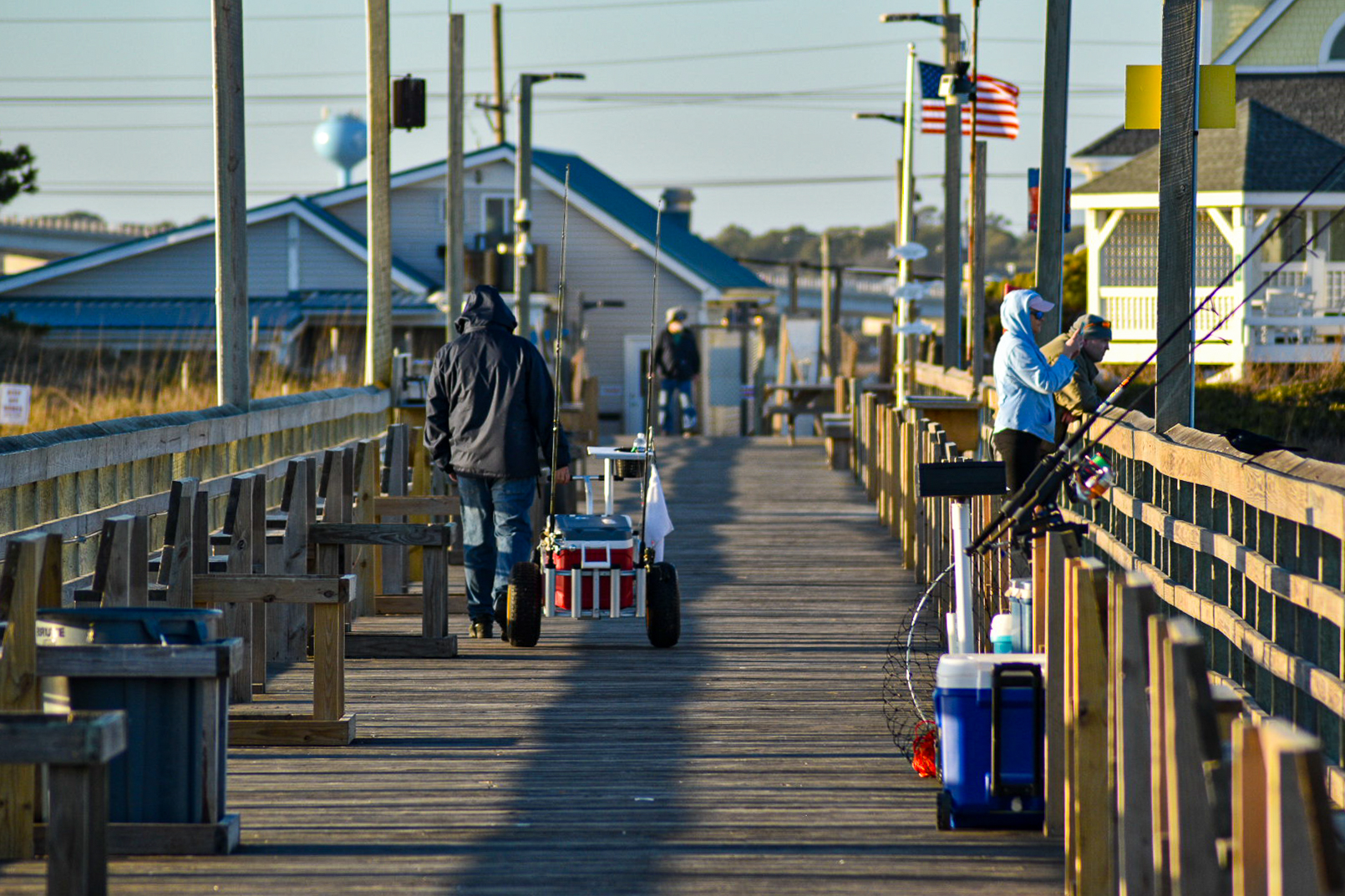 Two anglers on a pier at golden hour, one pulling a loaded cart